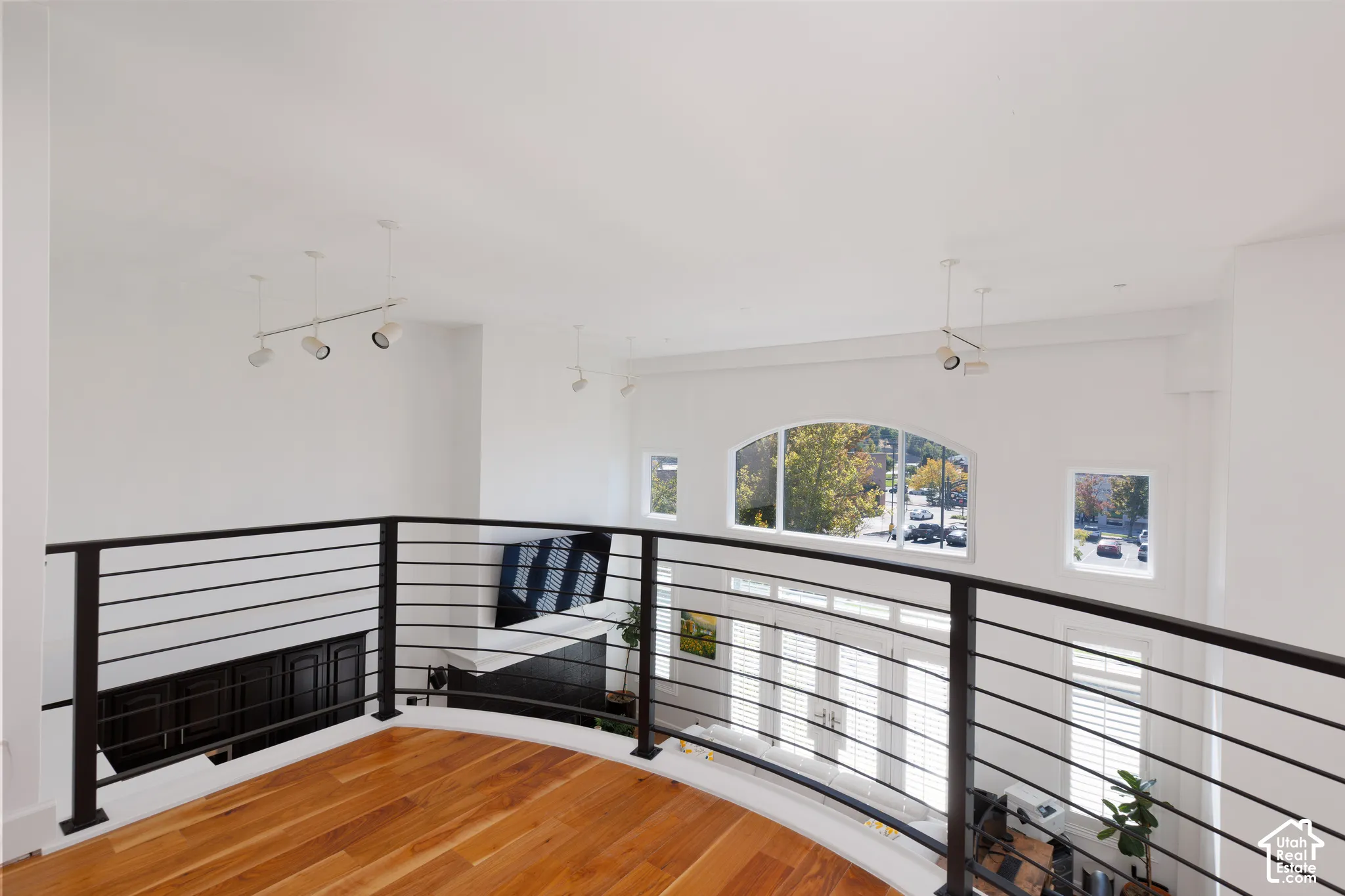 Loft area featuring wood-finish flooring, black metal railing, vaulted ceilings, and an arched window