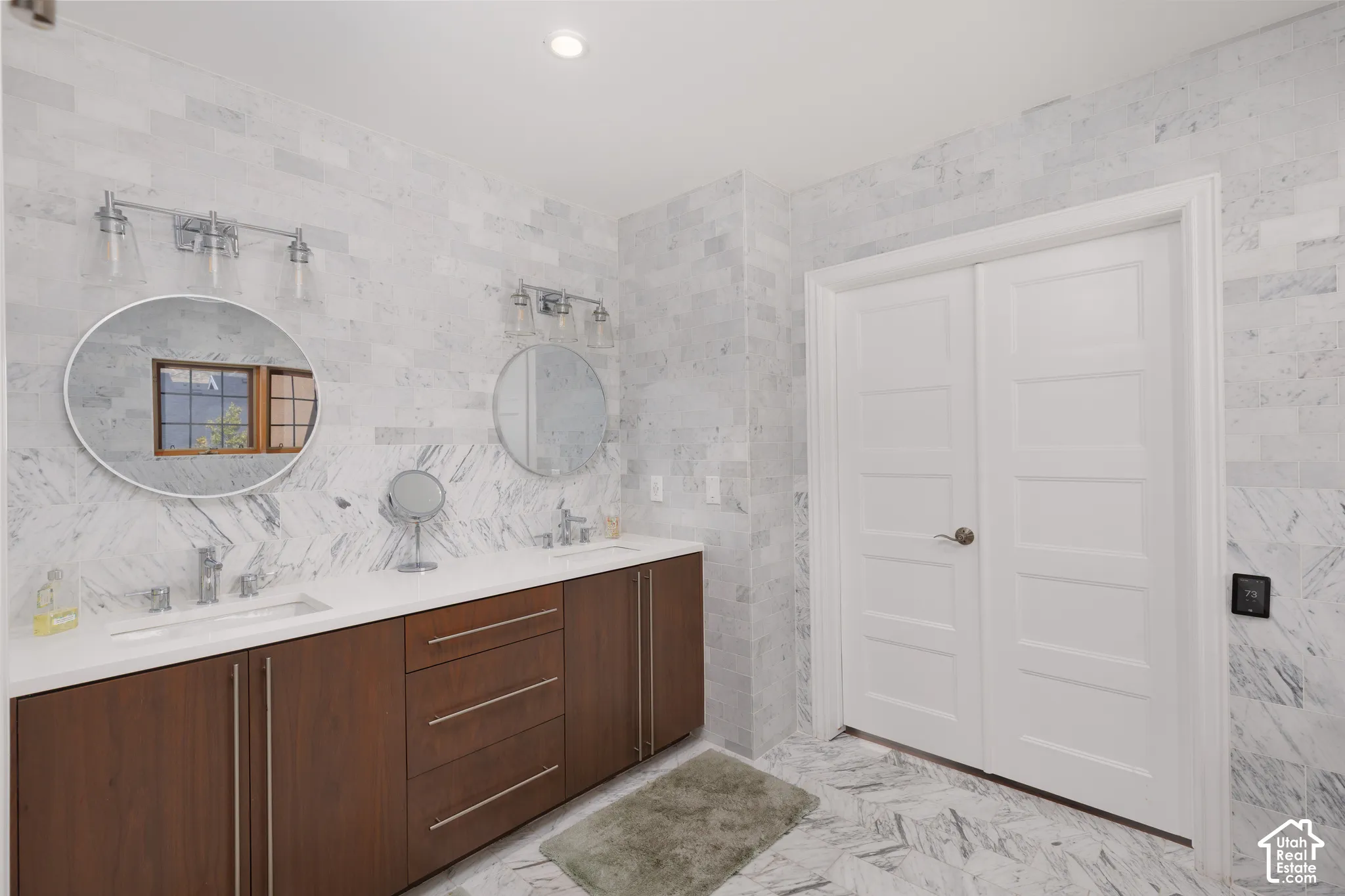 Double vanity with wood-finish cabinetry, circular mirrors, and a white countertop