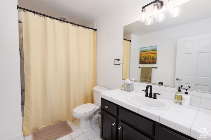 White tiled flooring, dark wood-finish vanity with silver hardware, white tiled countertop, undermount sink, and matte black faucet
