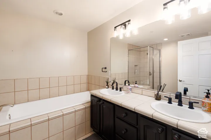 Dual vanity with dark cabinetry and tile countertop, featuring a built-in tub and a separate glass-enclosed shower