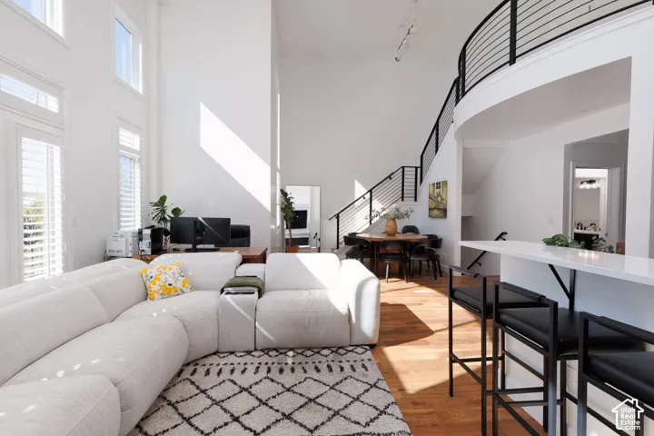 Two-story windows with plantation shutters, wood-finish flooring, two-story ceilings, a curved staircase with horizontal metal balusters, and a white countertop bar