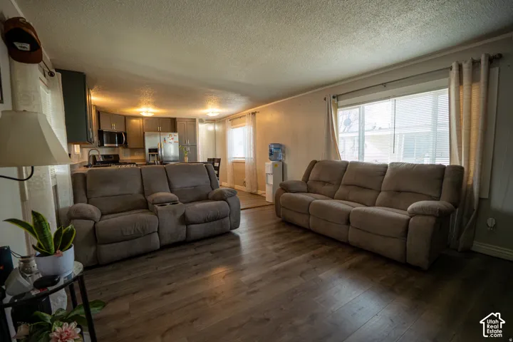 Wood-finish flooring throughout, bright window with blinds, recessed lighting in kitchen, dark wood-finish cabinetry, and stainless steel appliances