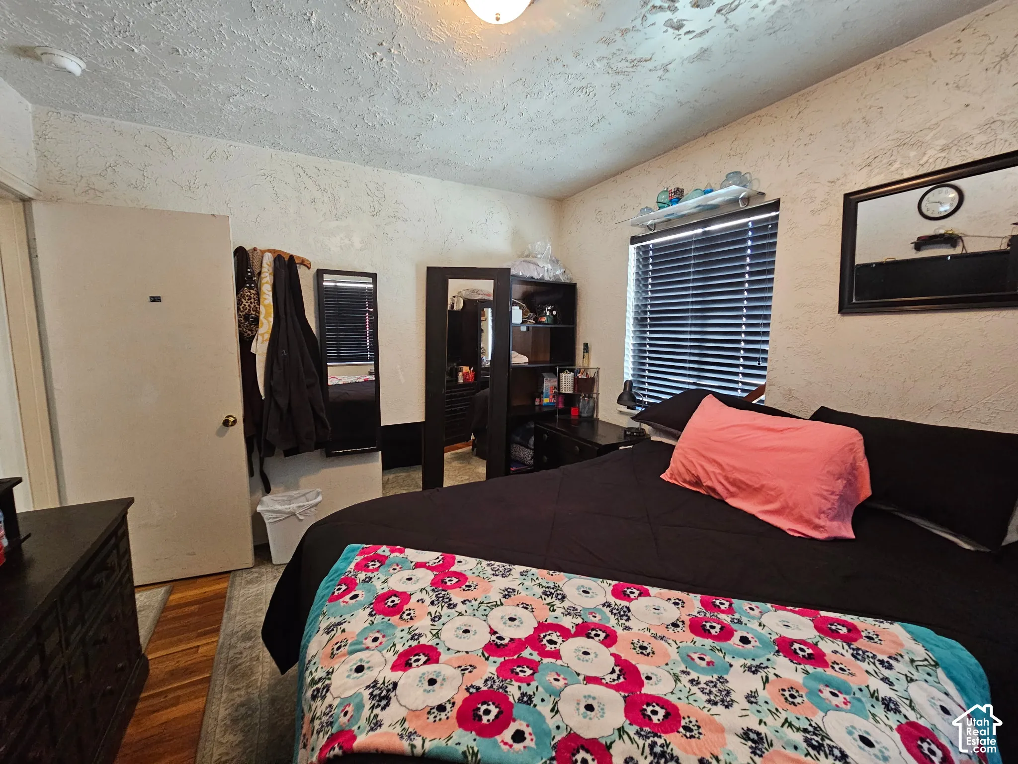 Textured wall and ceiling finishes, window with horizontal blinds, and warm-toned wood-finish flooring