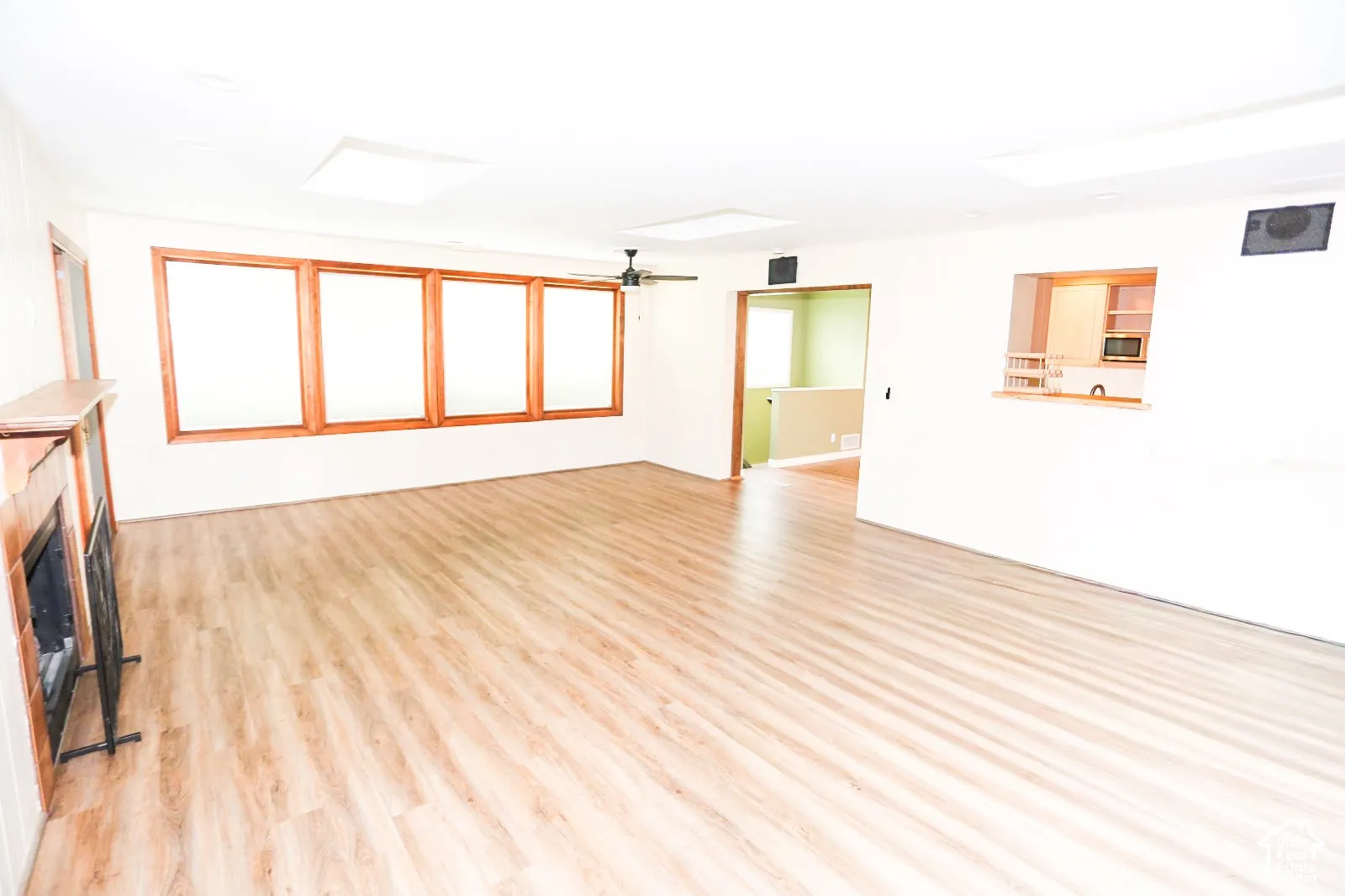 Spacious living area featuring wood-finish flooring, a fireplace with a wood mantle, and multiple windows with wood trim