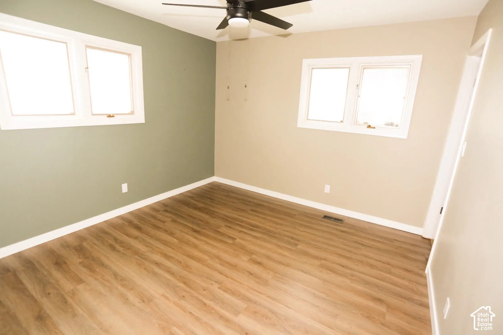 Wood-finish flooring, white trim, dual windows, and a ceiling fan with integrated lighting