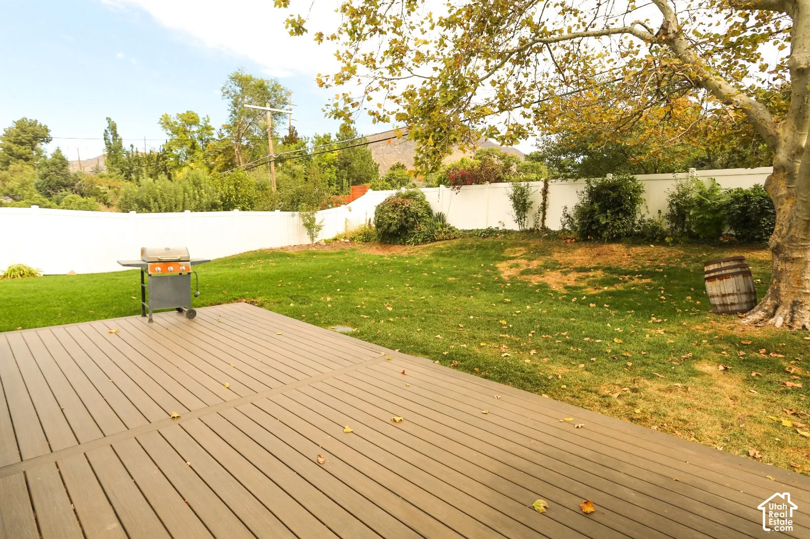 Expansive backyard featuring a composite deck, mature trees, manicured lawn, and a white privacy fence