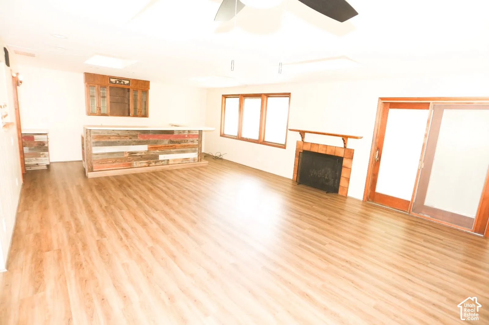 Wood-finish flooring throughout, integrated bar with reclaimed wood paneling, built-in display cabinetry, brick-surround fireplace with wood mantel, and sliding glass door