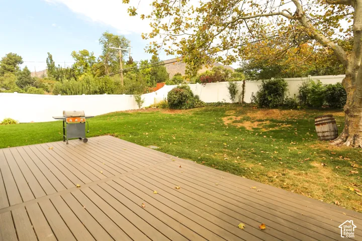 Expansive backyard featuring a composite deck, mature trees, manicured lawn, and a white privacy fence
