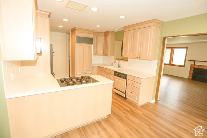 Light wood-finish cabinetry, integrated refrigerator, built-in cooktop, undermount sink with a gooseneck faucet, and wood-finish flooring