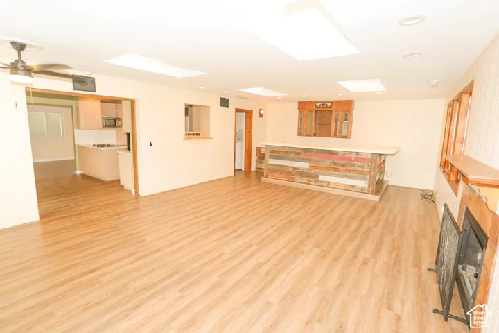 Spacious room with wood-finish flooring, a built-in wet bar with a countertop, a fireplace with a wood mantel, and multiple skylights