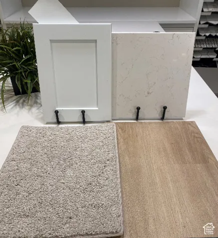 White shaker cabinet door sample, light-toned stone slab, neutral-toned carpet sample, and wood-finish flooring sample
