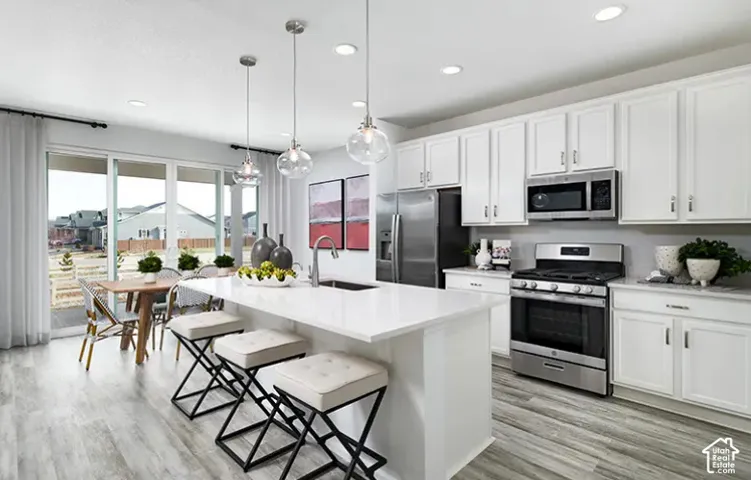White cabinetry with stainless steel appliances, wood-finish flooring, recessed lighting, and a kitchen island with pendant lighting