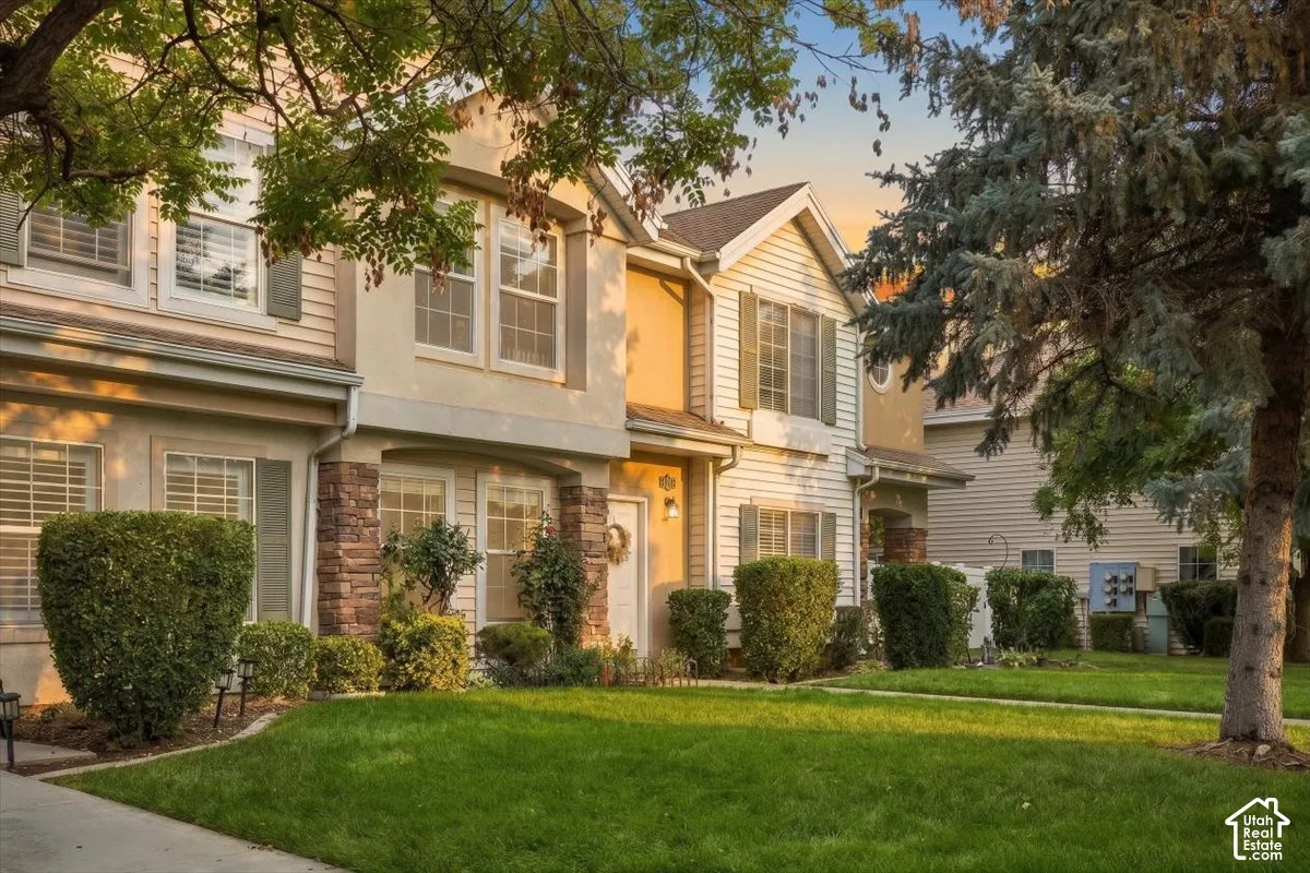 Stucco and siding exterior with stone veneer accents, dual-pane windows, and a landscaped front yard with mature shrubbery and trees
