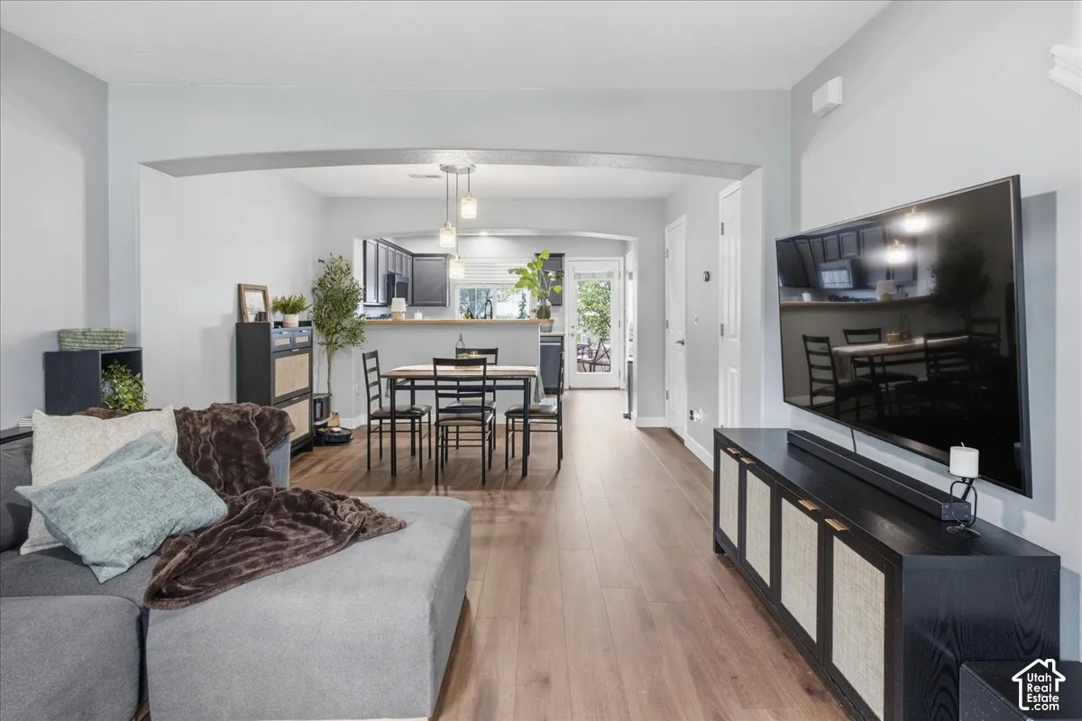 Wood-finish flooring throughout, light gray wall color, arched doorway, recessed lighting, and a kitchen pass-through