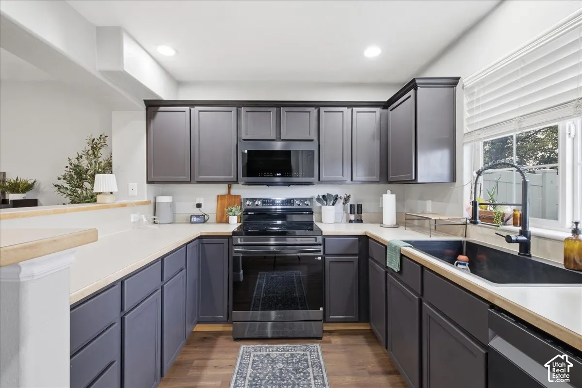Modern kitchen featuring dark cabinetry, light countertops, wood-finish flooring, a stainless steel range, and an undermount sink