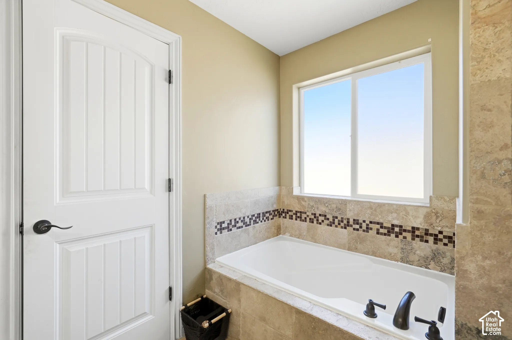 Built-in soaking tub with tile surround, decorative mosaic tile accent, and a large window