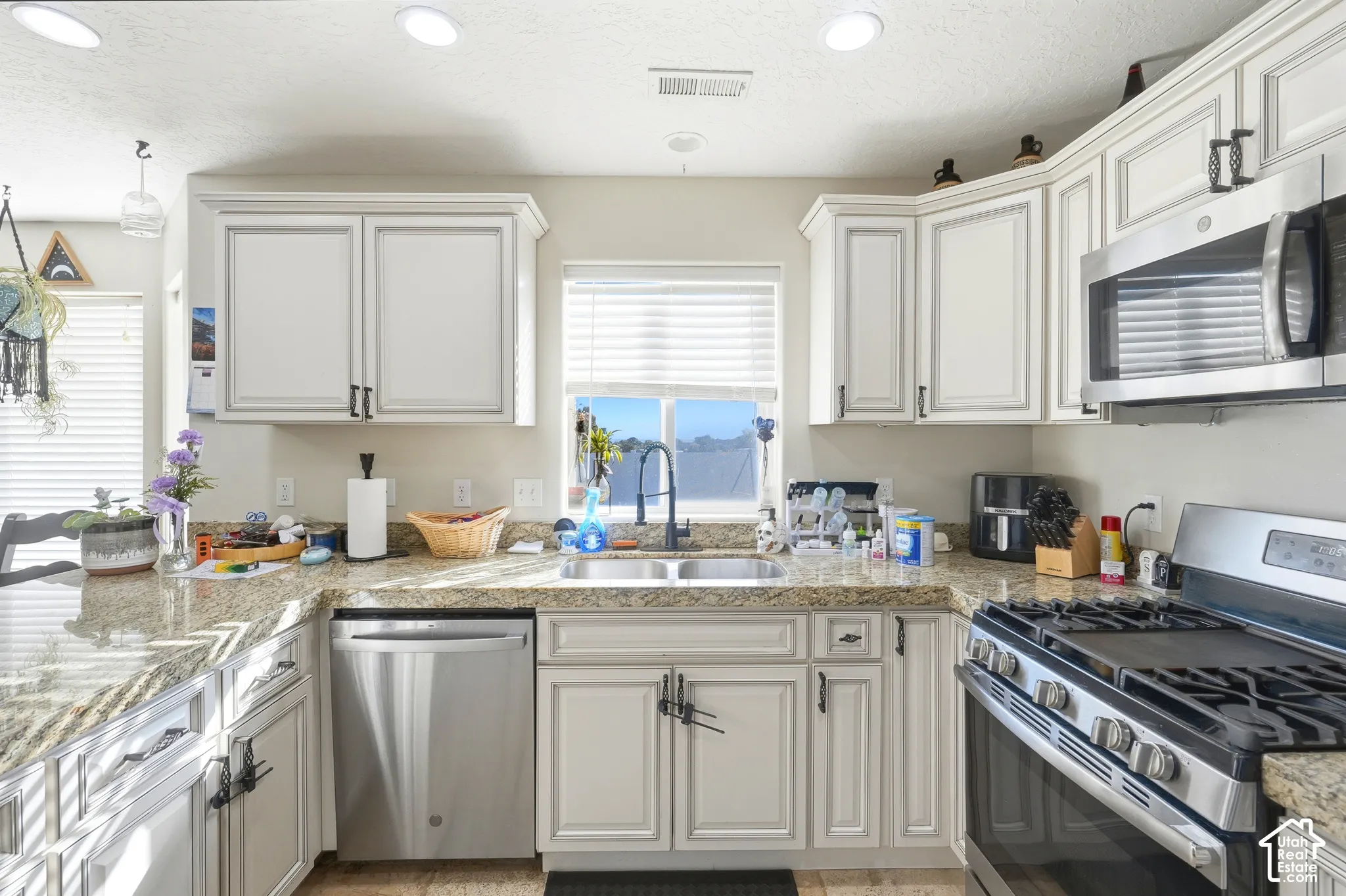Kitchen featuring light-toned cabinetry, stone-finish countertops, stainless steel appliances, a double basin sink, and recessed lighting