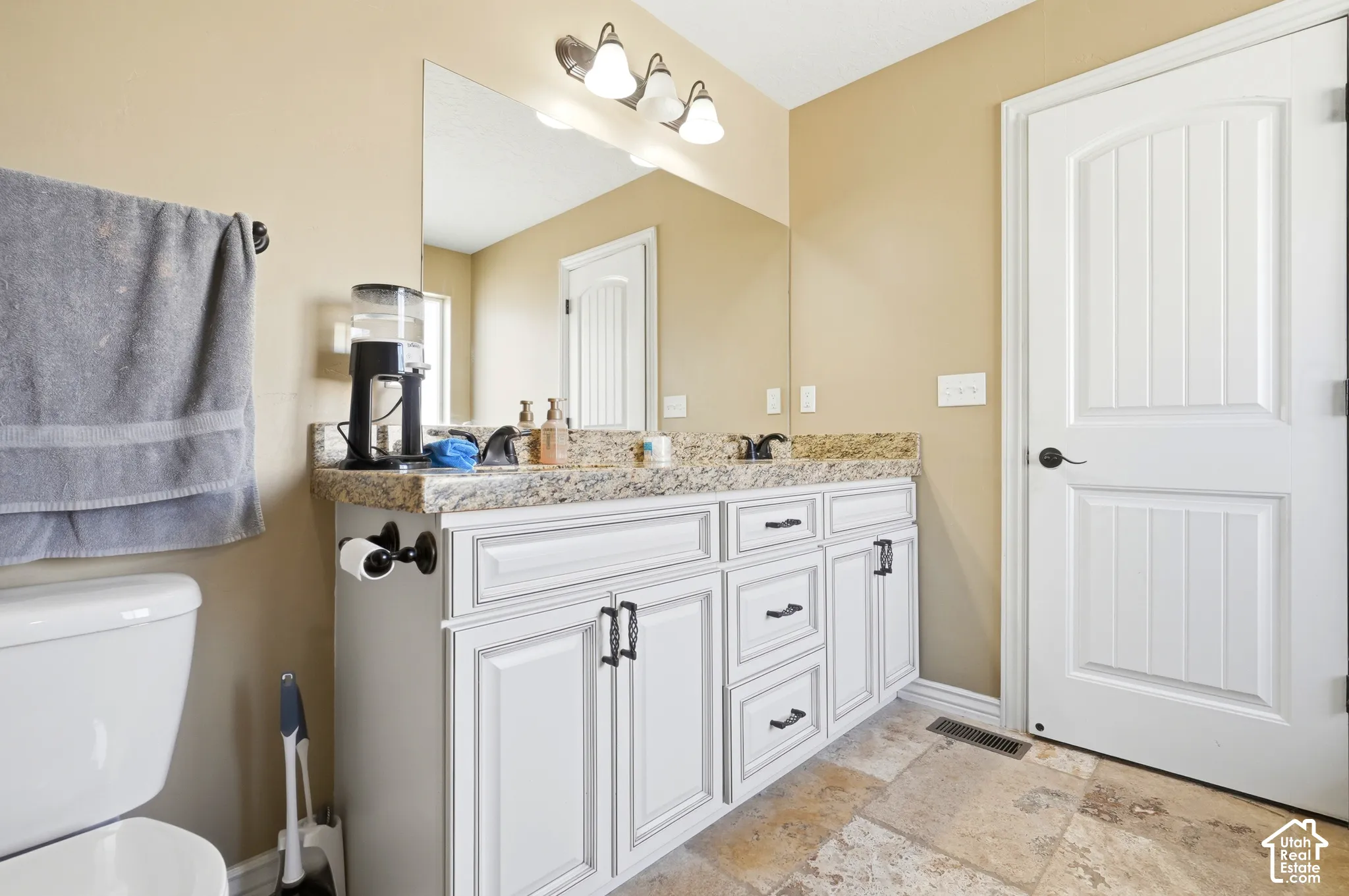 Dual vanity with granite countertop, white cabinetry with dark hardware, large wall-mounted mirror, and tile flooring