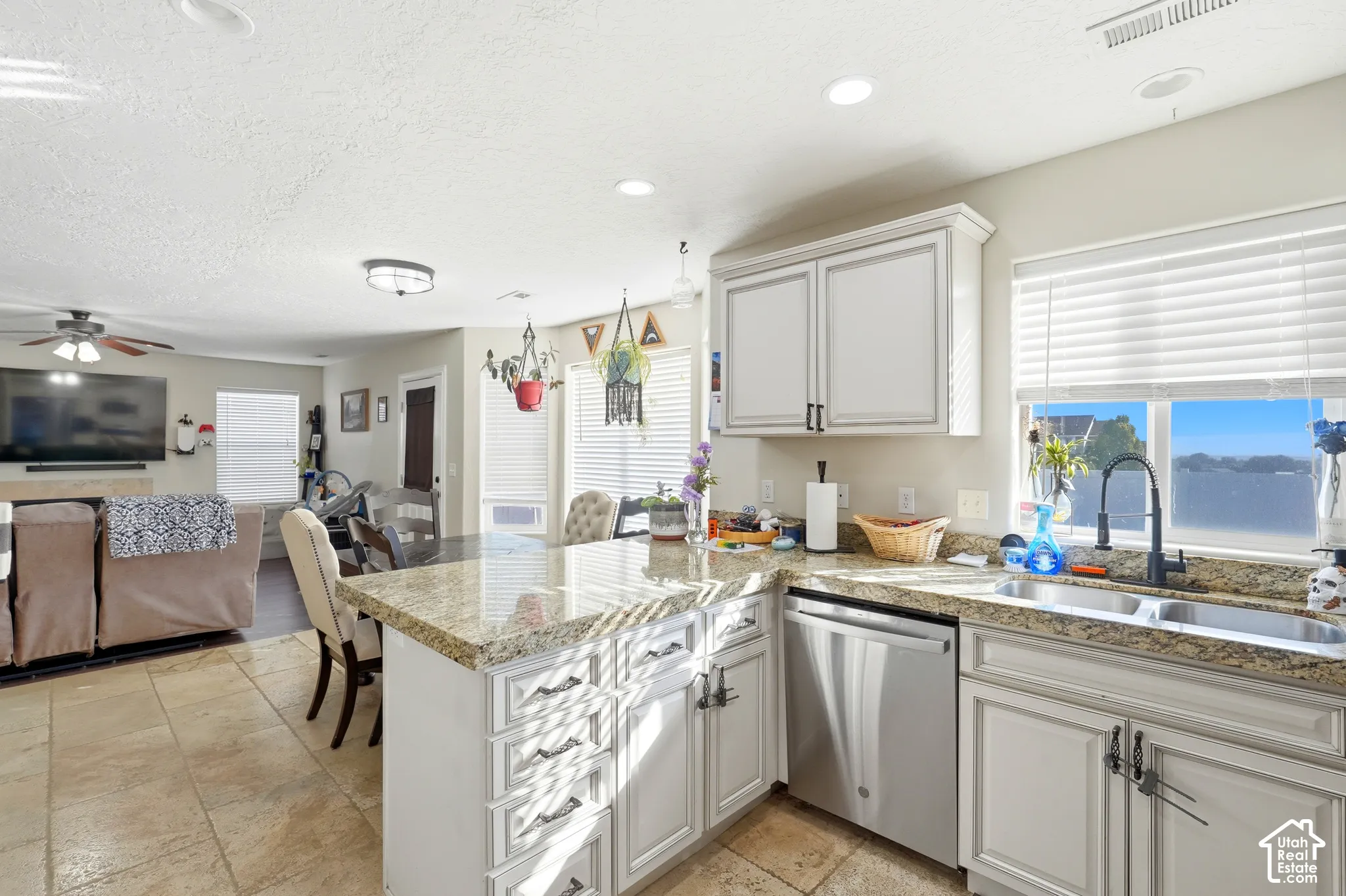 Kitchen featuring a large window, stainless steel dishwasher, an undermount double basin sink with a matte black faucet, light-toned cabinetry, and stone countertops