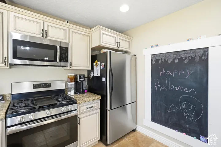 Stainless steel appliances, built-in microwave, gas range, cream-finish cabinetry, and granite-style countertops