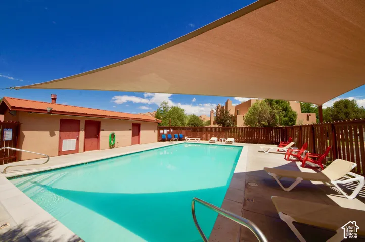 Rectangular swimming pool with surrounding concrete decking, complemented by a large shade sail overhead