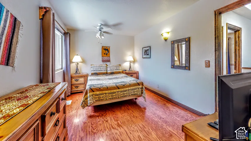Wood-finish flooring with a ceiling fan, wall sconces, and a window