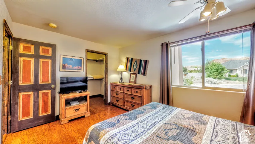 Wood-finish flooring, built-in open closet, large window, and ceiling fan with integrated lighting