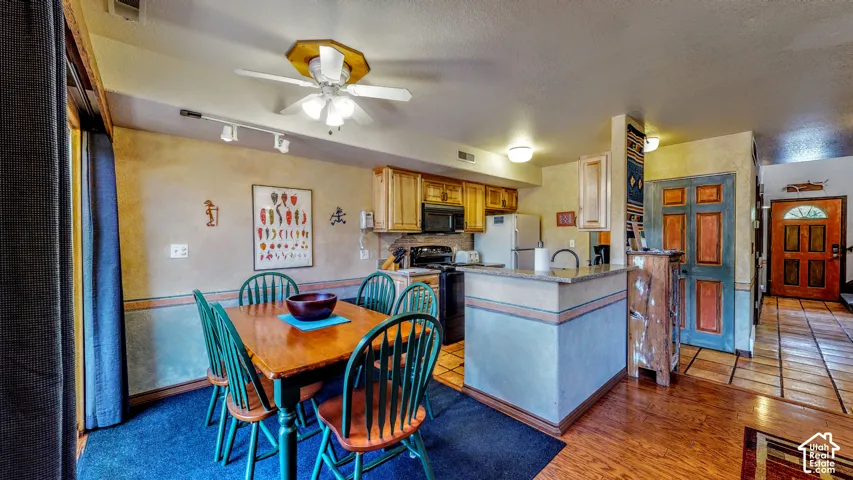 Open-concept kitchen and dining area featuring wood-finish cabinetry, a ceiling fan, track lighting, a breakfast bar with a solid surface countertop, and tile flooring in the kitchen area