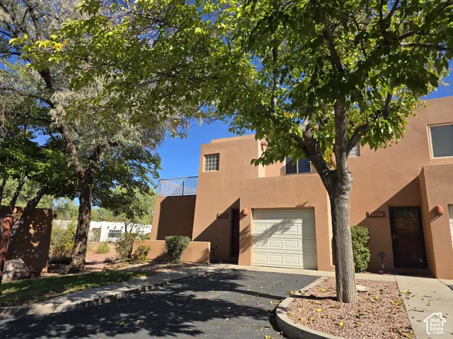 Stucco exterior finish, attached garage with panel door, front entry with security door, upper-level balcony with metal railing, and a decorative glass block window