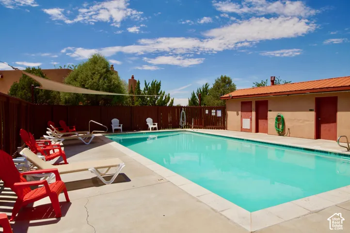 Outdoor swimming pool with concrete decking, a privacy fence, and a shade sail
