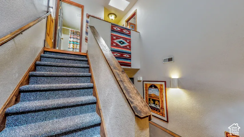 Staircase featuring wood-finish handrails and blue carpeting, with white wall sconces providing illumination
