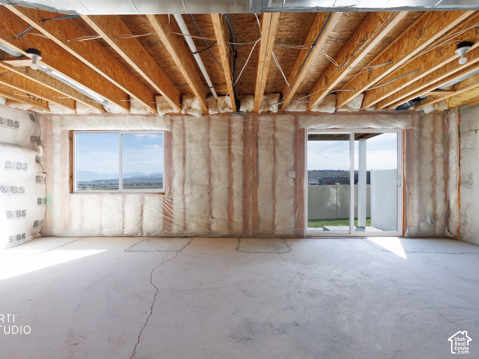 Unfinished basement featuring exposed wood ceiling joists, concrete flooring, exterior window, and a sliding glass door