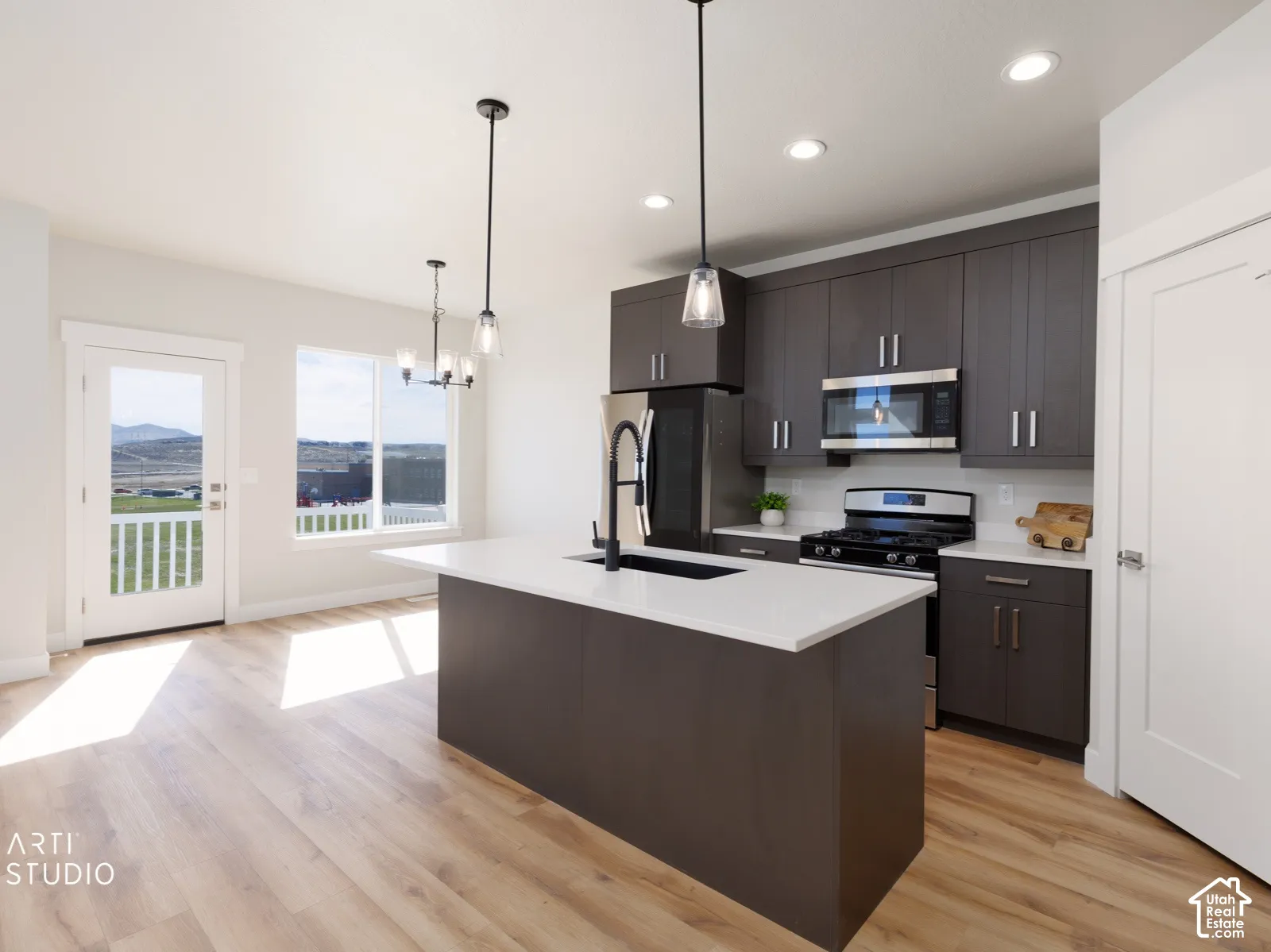 Modern kitchen featuring dark wood-finish cabinetry, stainless steel appliances, a center island with a white countertop, and wood-finish flooring