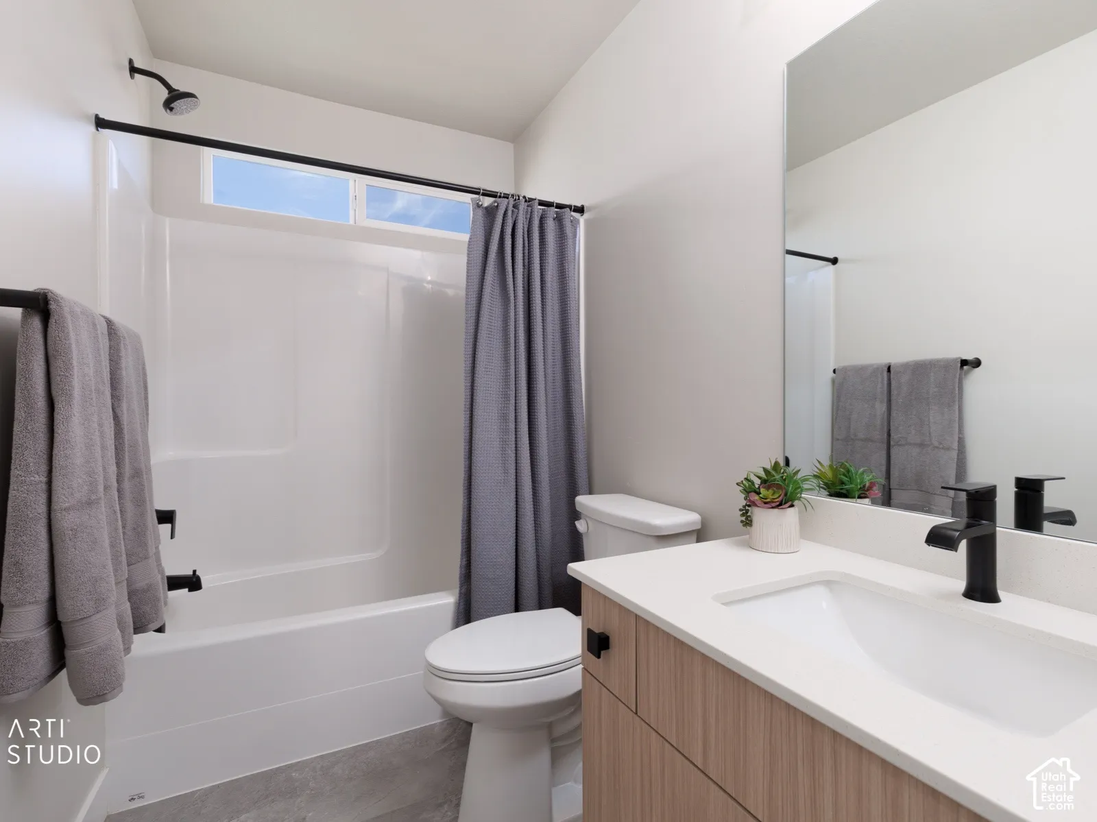 White shower/tub combination with black fixtures, transom window, and grey shower curtain