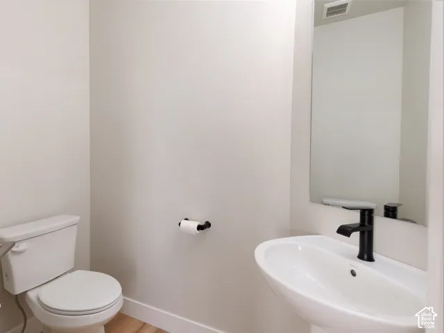 Pedestal sink with a matte black faucet, wall-mounted mirror, and wood-finish flooring