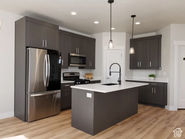 Modern kitchen featuring matte dark gray cabinetry, stainless steel appliances, a central island with a white countertop and dark faucet, wood-finish flooring, and pendant lighting