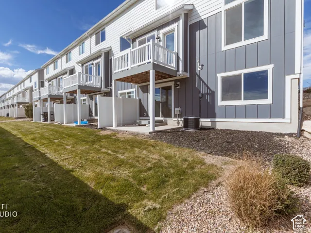 Exterior featuring board-and-batten siding, multiple balconies with white railings, ground-level patios, and a manicured lawn area