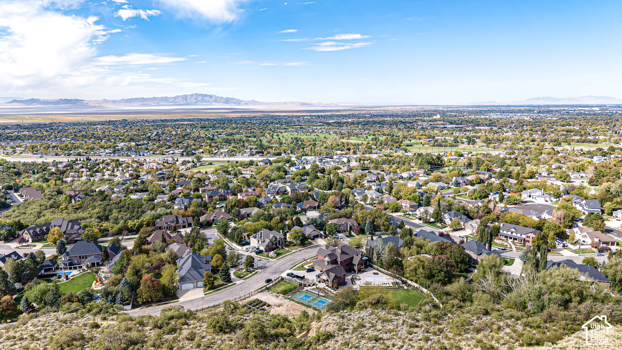 Expansive residential area with a prominent golf course, distant mountain range, and scattered mature trees