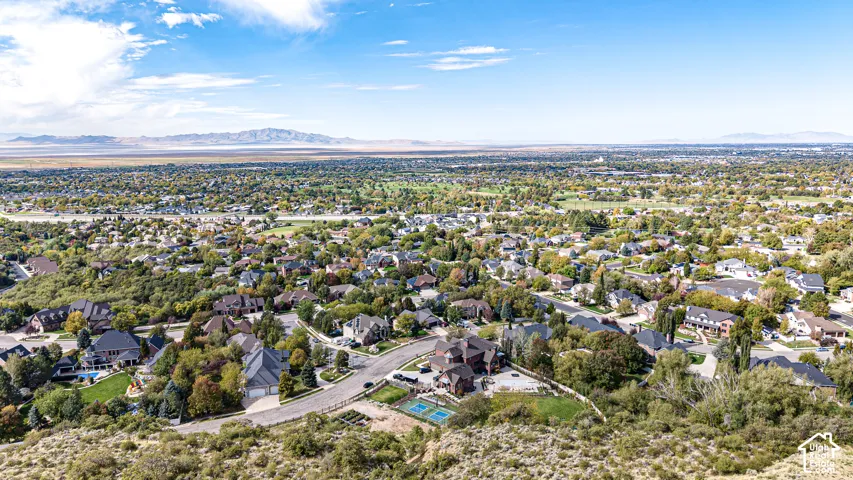 Expansive residential area with a prominent golf course, distant mountain range, and scattered mature trees