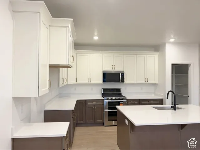 Kitchen featuring two-tone shaker-style cabinetry, quartz countertops, stainless steel appliances, a center island with an undermount sink and matte black faucet, and a walk-in pantry