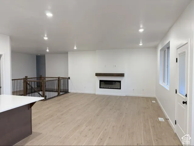 Open-concept living space featuring wood-finish flooring, recessed lighting, a linear fireplace with a wood mantel, and a dark metal railing