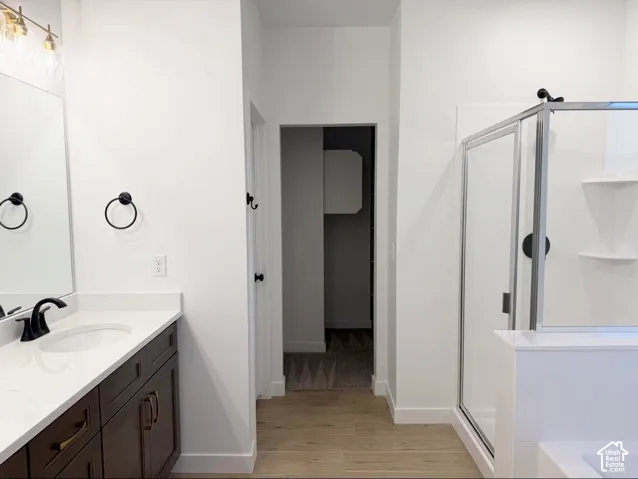 Bathroom featuring a dark wood-finish vanity, light-toned countertop with integrated sink, glass-enclosed shower with matte black fixtures, and wood-finish flooring
