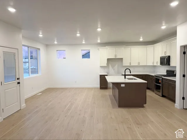 Kitchen featuring two-tone cabinetry, quartz countertops, a central island with a matte black faucet, and light-tone wood-finish flooring throughout