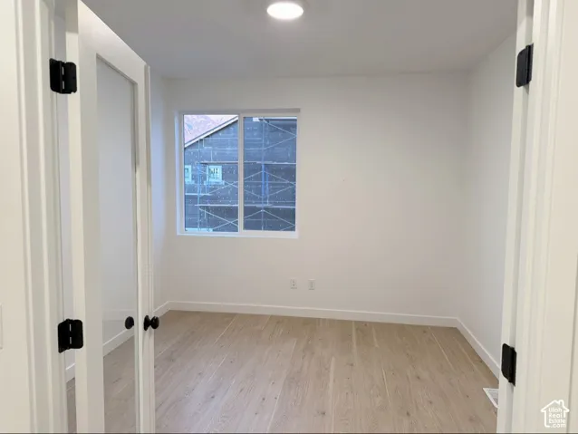 Room featuring white walls, wood-finish flooring, a sliding window, and double doors with matte black hardware