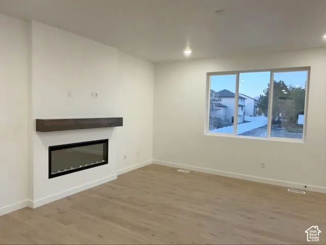 Linear electric fireplace with a wood-finish mantel, wood-finish flooring, recessed lighting, and large windows
