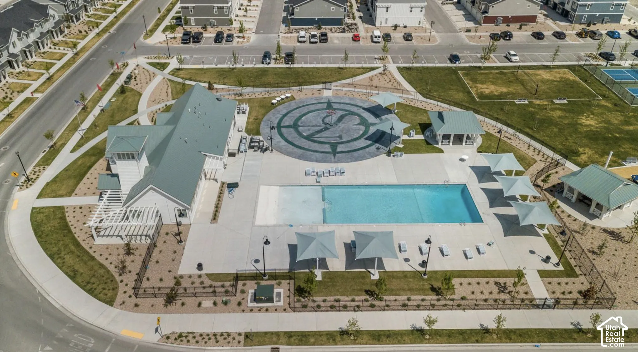 Community clubhouse with an outdoor swimming pool, surrounded by paved lounge areas, covered pergolas, and landscaped grounds