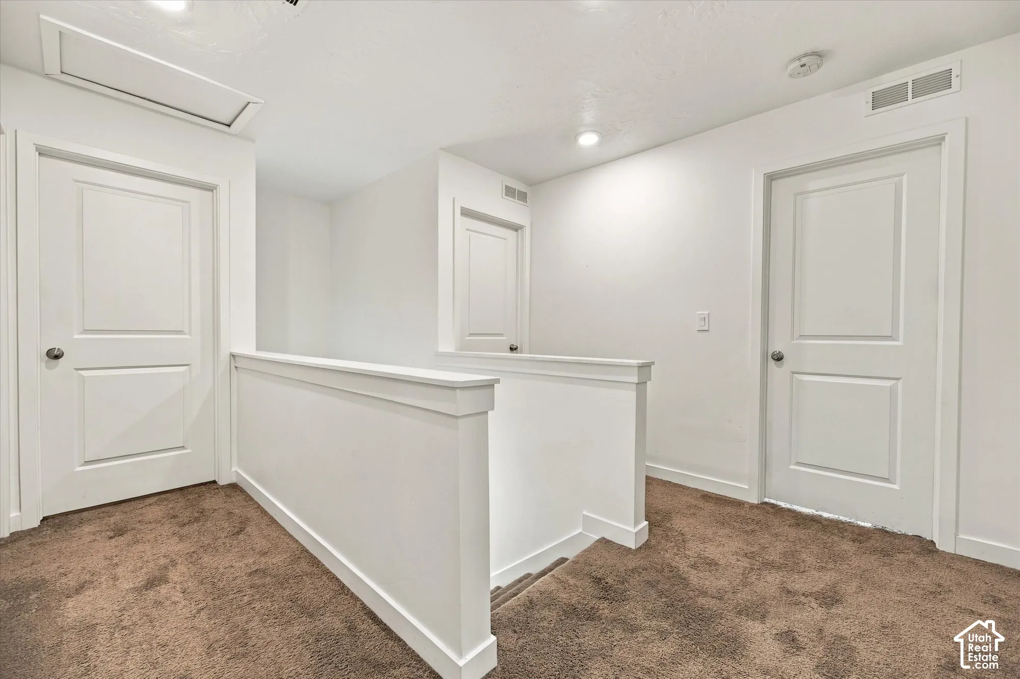 Carpeted landing featuring white doors, recessed lighting, and a white half-wall railing