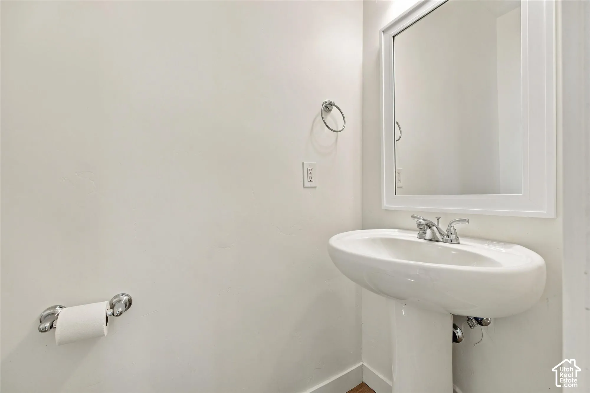 White pedestal sink with a chrome faucet, illuminated by an overhead light, and a framed mirror