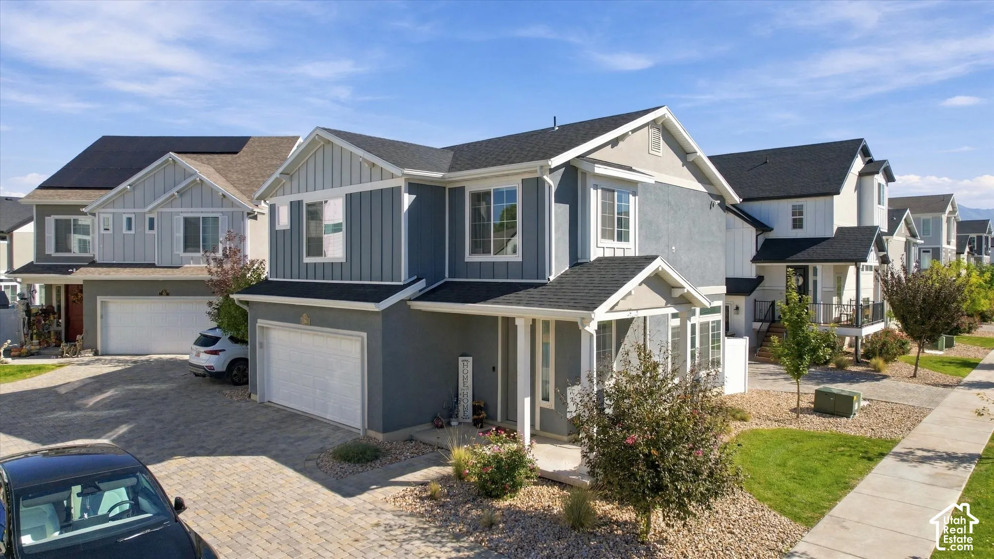 Contemporary exterior with gray siding and white trim, featuring a paved driveway, attached garage, and landscaped front yard