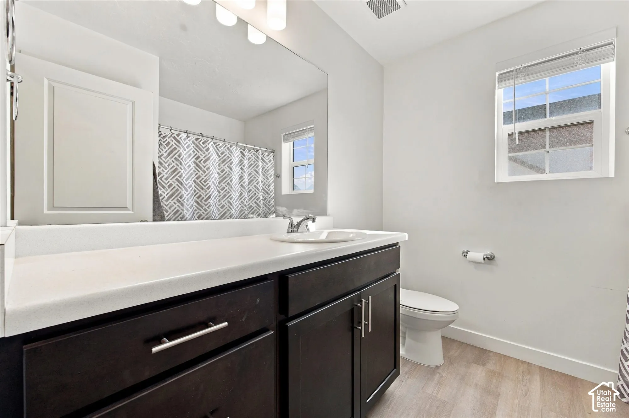 White walls with a window, wood-finish flooring, dark wood-finish vanity with white countertop, and a white toilet